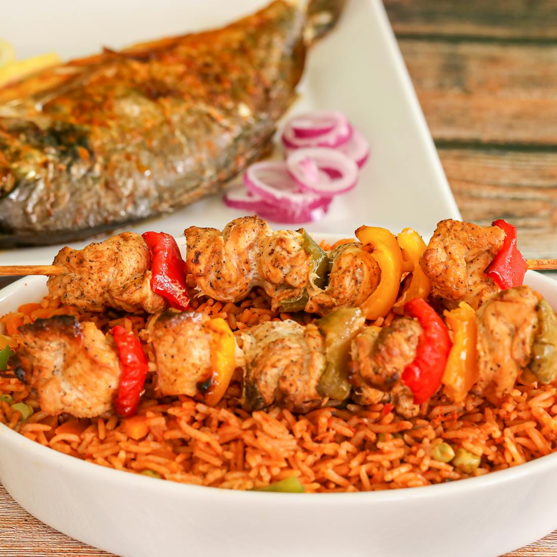 Plate of jollof rice with chicken skewers and grilled fish